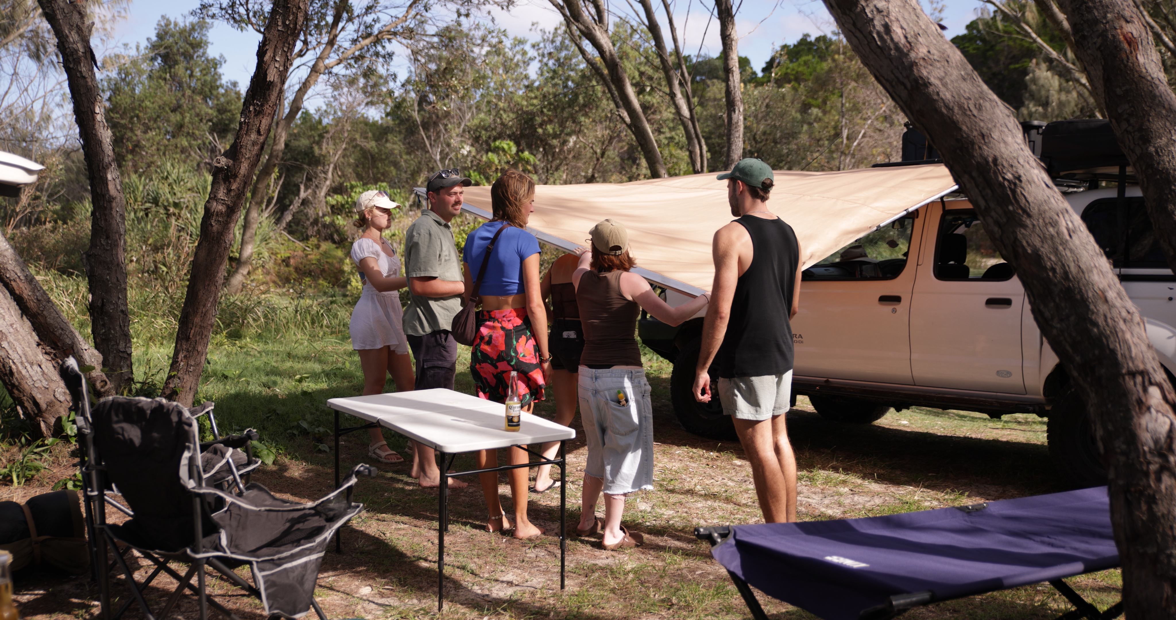 Group around a campfire at night with rooftop tents and drinks
